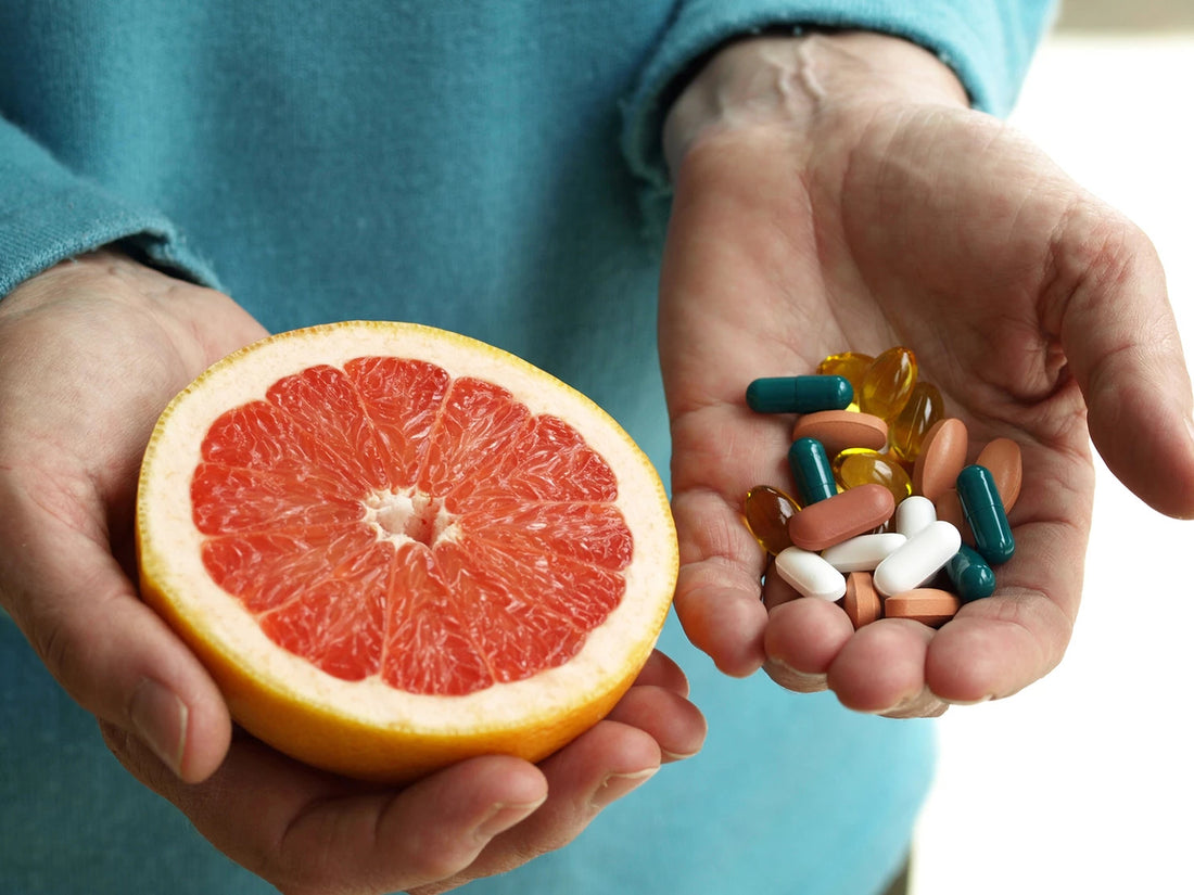 A hand with half a grapefruit and another with handful of medicine pills