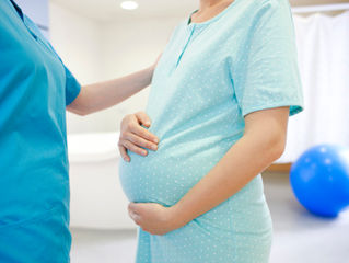 Pregnant woman in blue hospital gown holding her belly